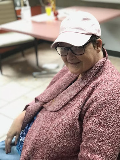A woman smiling while wearing a cap and glasses, enjoying her time indoors.
