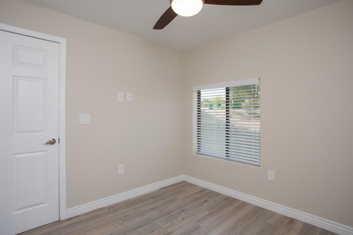 An empty room with a ceiling fan, hardwood floors, and a window with blinds letting in natural light.