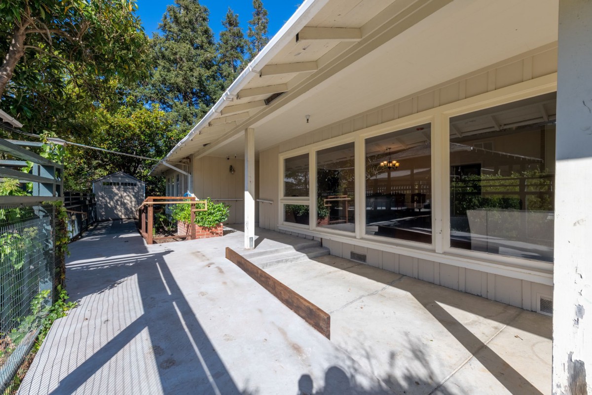 A sunny view of a house exterior with large windows and a patio.