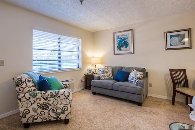 A cozy living room with a gray sofa, patterned armchair, lamp, and wall art.