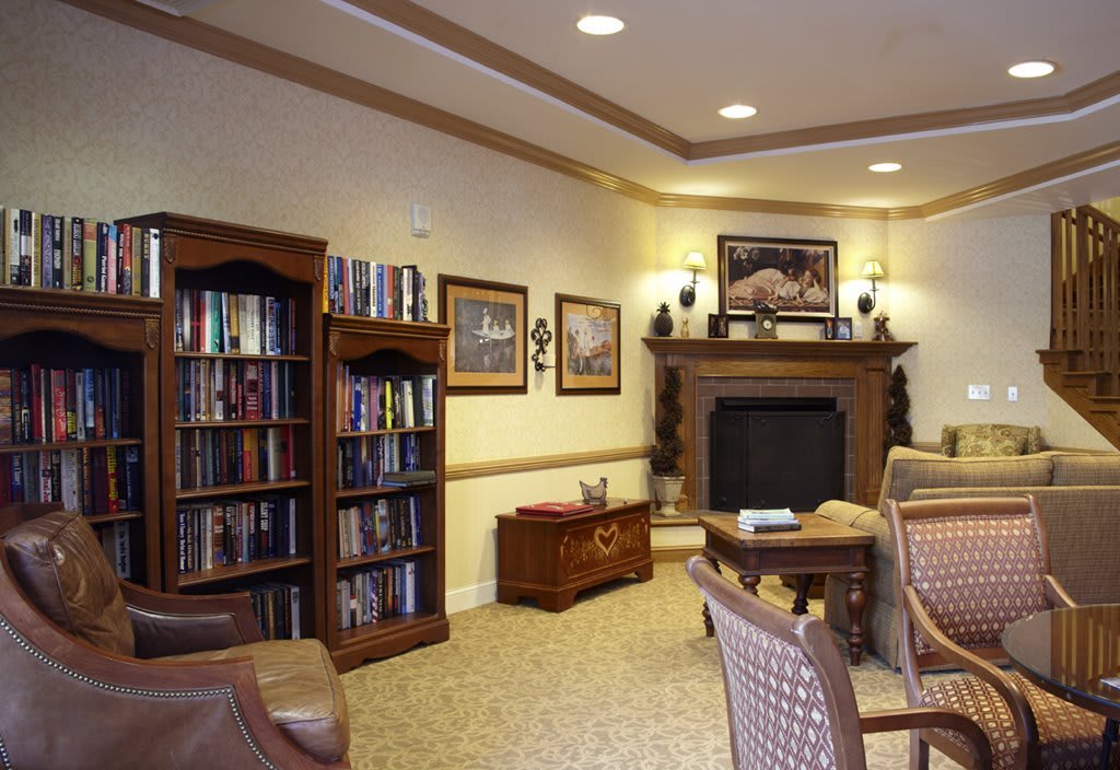 A cozy library room with bookshelves, a fireplace, and comfortable seating.