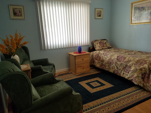 A cozy bedroom featuring a single bed, green armchairs, and light blue walls.