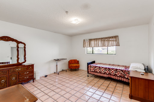 A spacious room featuring a bed, a wooden chest of drawers, and a window with curtains.