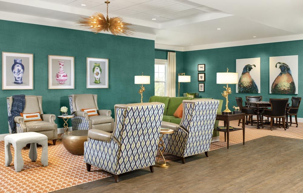 A stylishly decorated living room with patterned armchairs, a green sofa, and elegant artwork on teal walls.