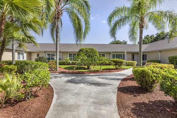 A well-maintained residential building surrounded by landscaped gardens and palm trees on a sunny day.
