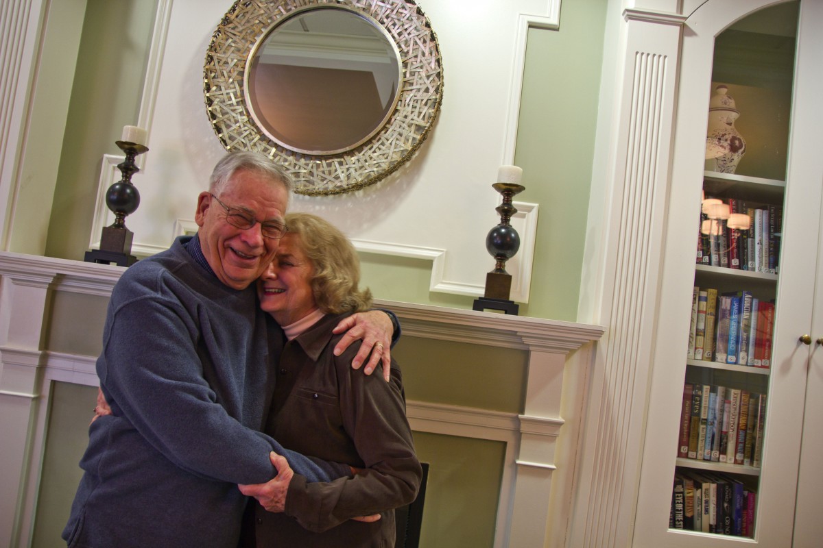 A happy couple embracing in front of a fireplace with decorative items.