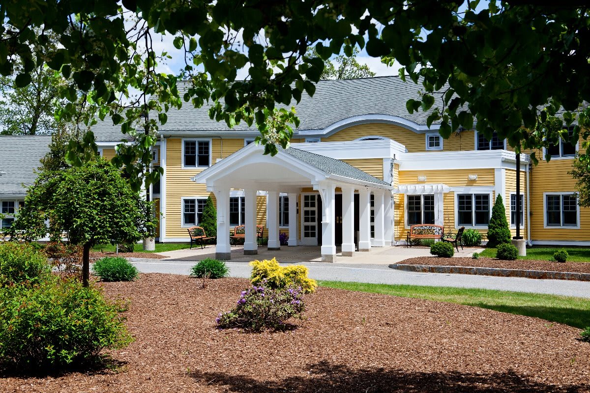A sunny view of a large yellow house with a welcoming entrance and well-maintained garden.