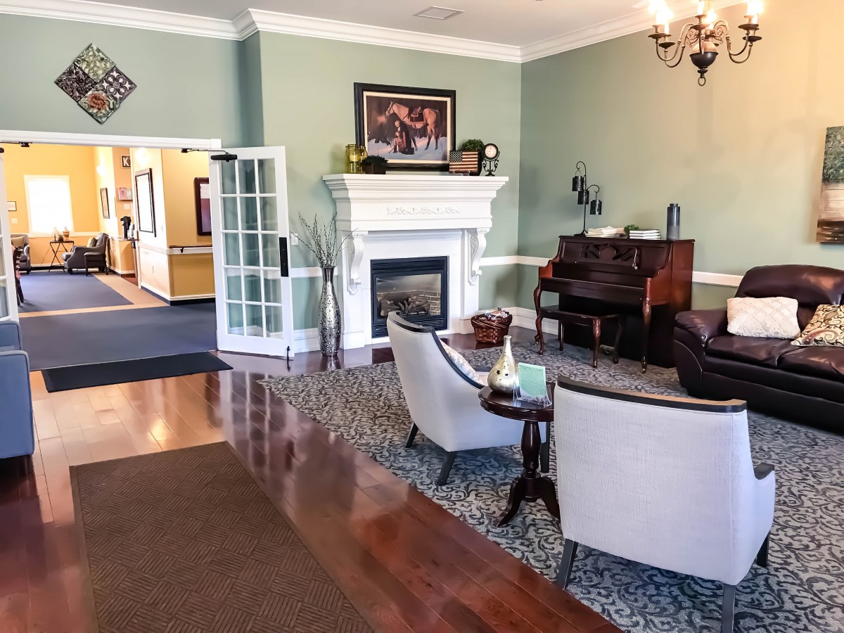 A cozy living room with a fireplace and piano, featuring comfortable chairs and elegant decor.