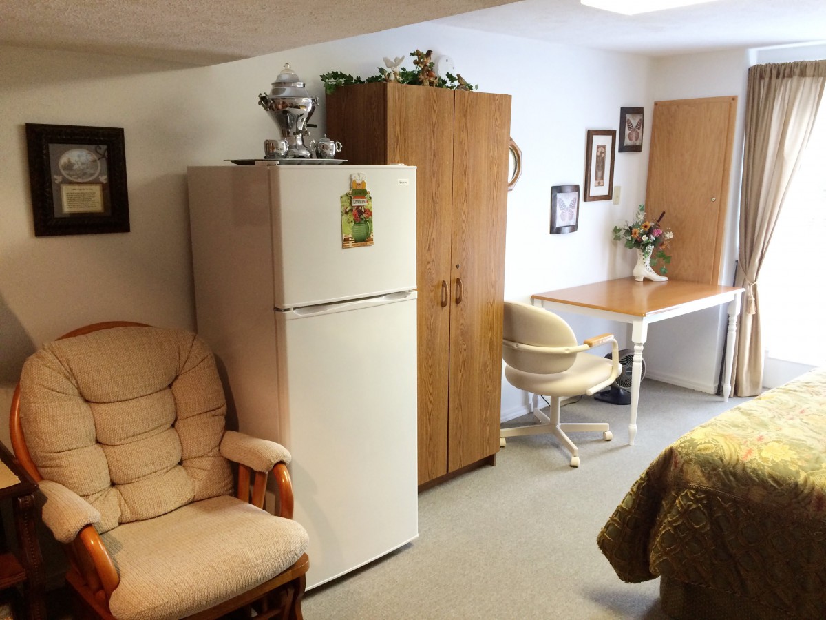 A cozy living area featuring a refrigerator, armchair, and desk with decor.