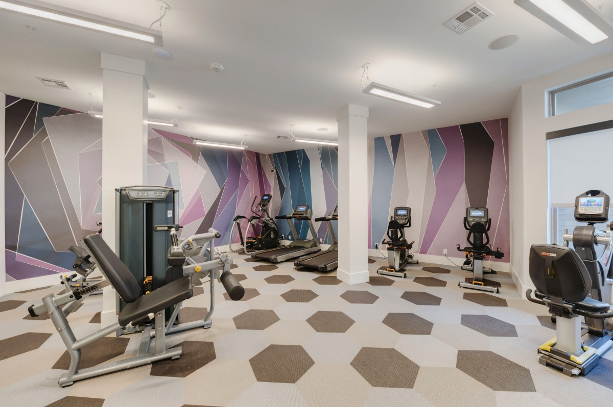 A modern indoor gym featuring various exercise machines and vibrant wall designs.