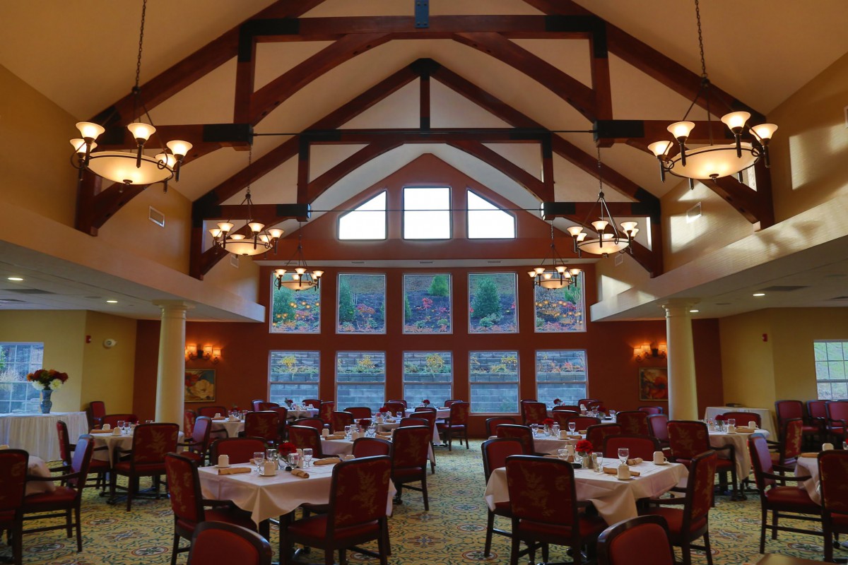 A spacious dining room with high ceilings and large windows, featuring elegantly set tables and chairs.