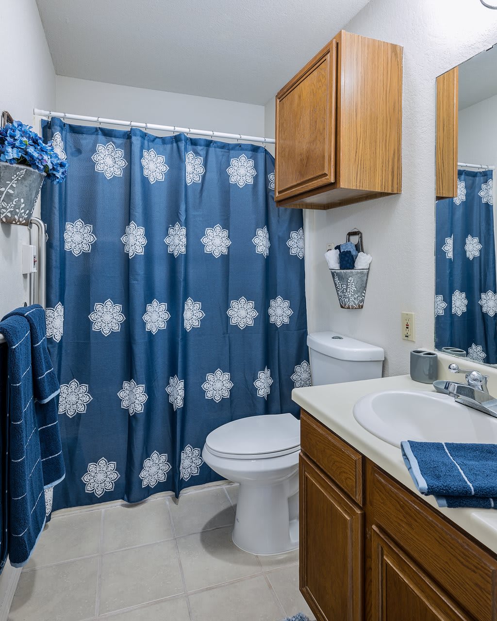 A bathroom with blue and white snowflake-themed decor, featuring a shower curtain, sink, cabinet, and toilet.