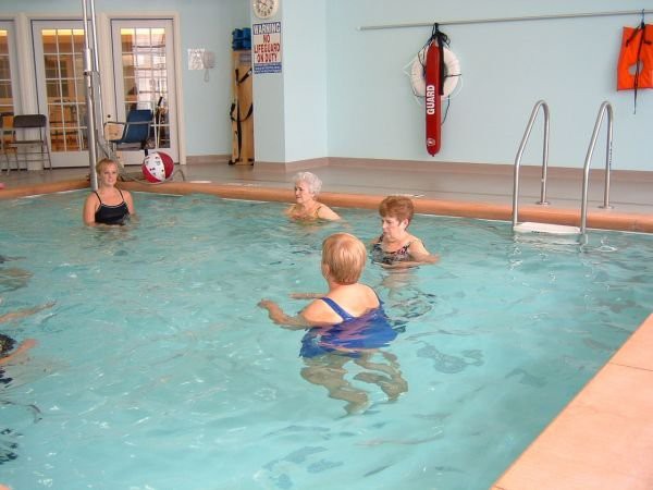 A group of seniors participating in a water aerobics class in an indoor swimming pool.
