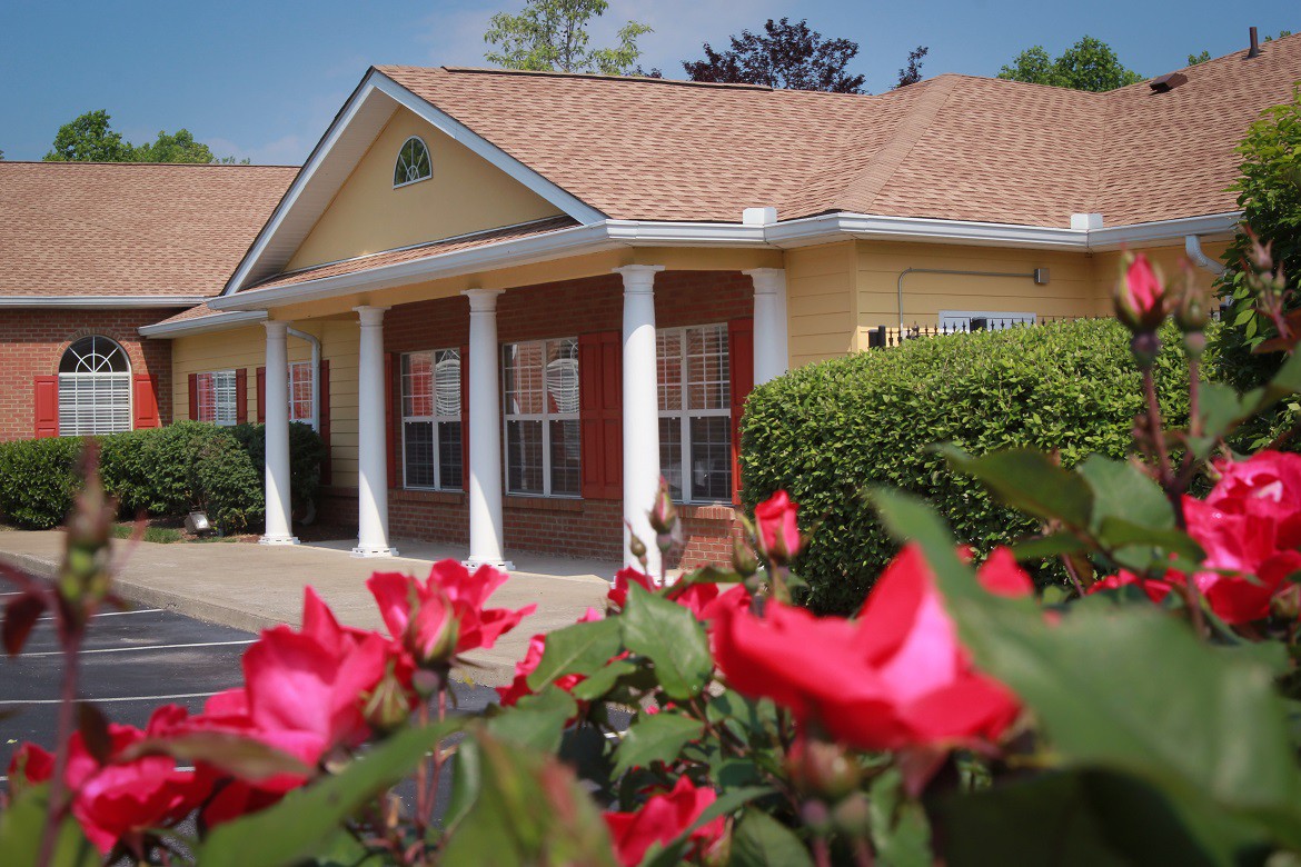A charming building with white columns, surrounded by vibrant red flowers on a sunny day.