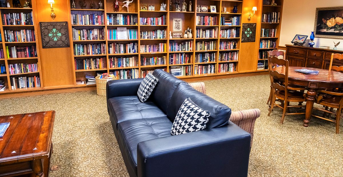 A cozy reading area featuring a black sofa with patterned cushions in front of a wall of bookshelves.