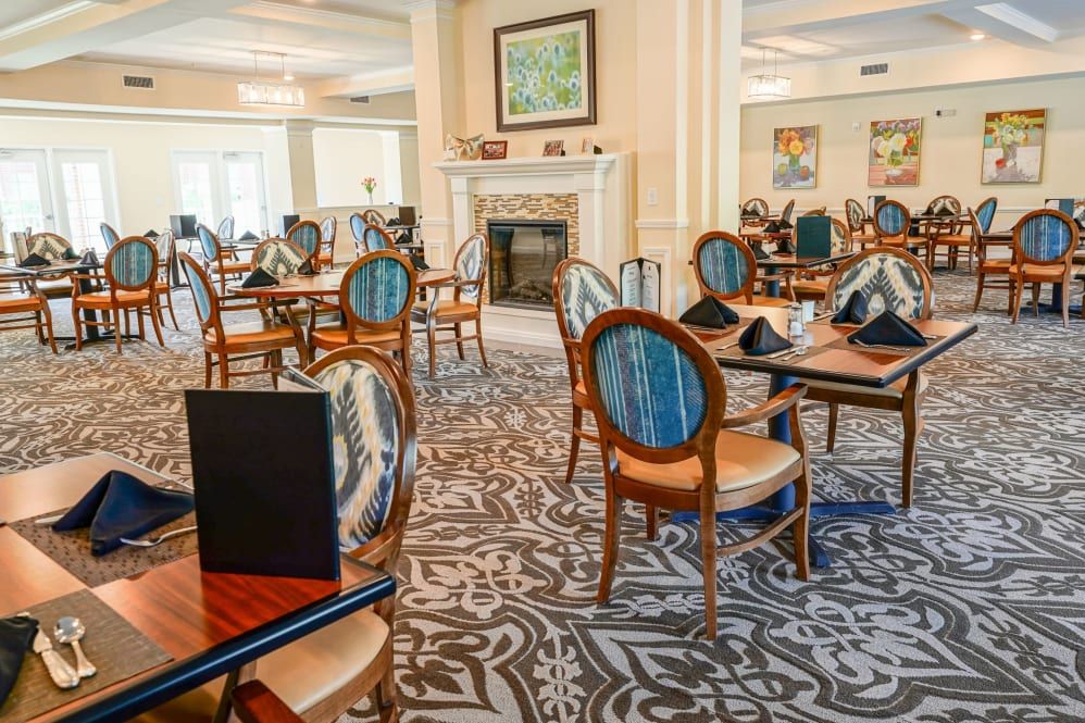 An elegant dining area with neatly arranged tables and chairs, featuring a patterned carpet and a fireplace.