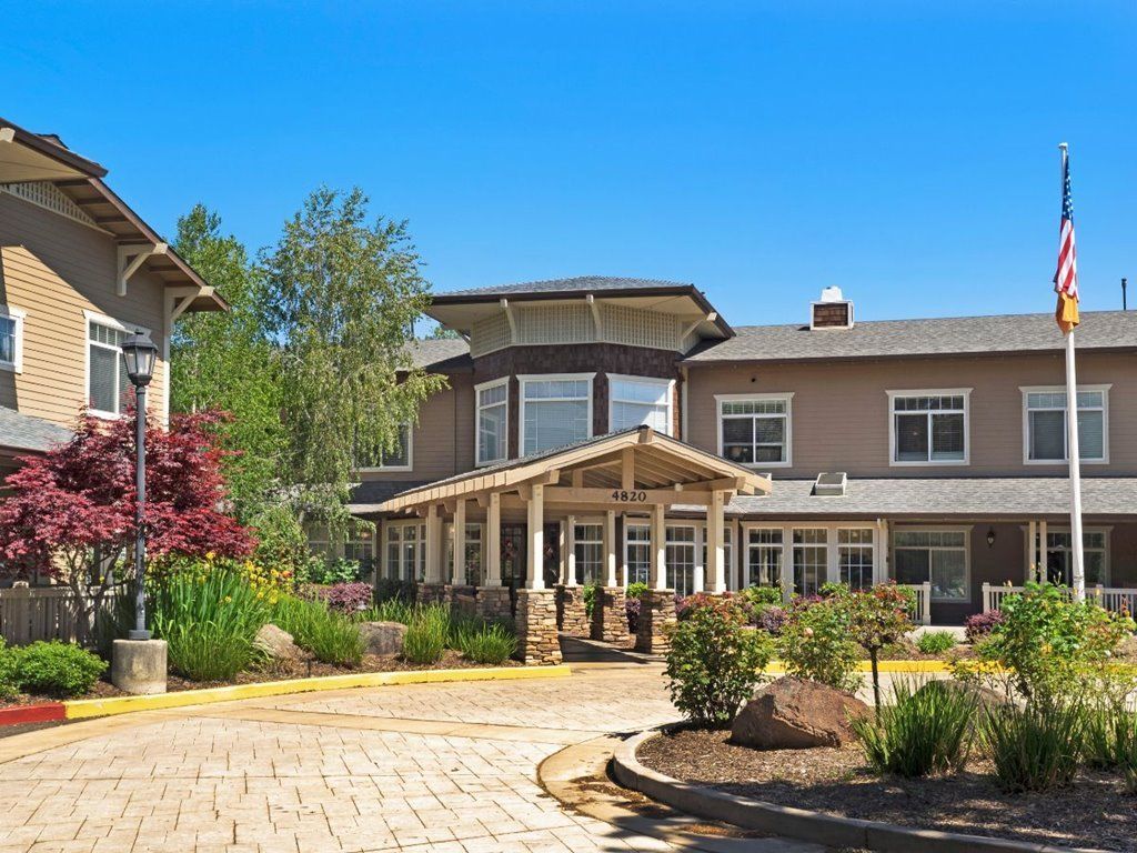 Exterior of a residential building with a landscaped garden and driveway on a sunny day.