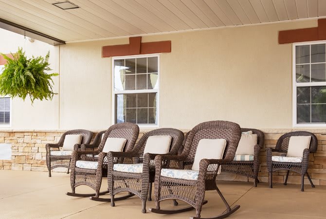 A row of wicker rocking chairs with cushions on a porch.