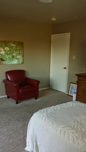 A cozy bedroom corner with a red armchair and wall art.