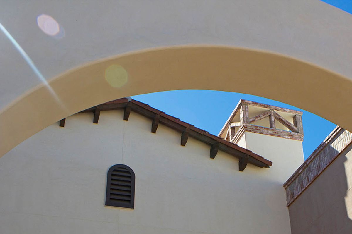 A view of architectural details featuring an arch, roof, and vent against a clear blue sky.