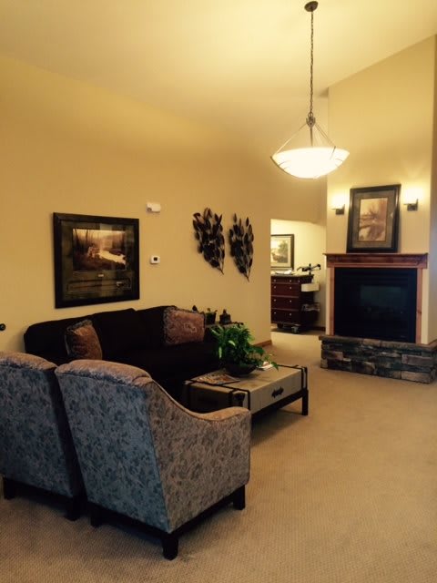 A cozy living room with a sofa, armchair, and fireplace, adorned with artwork and an indoor plant.