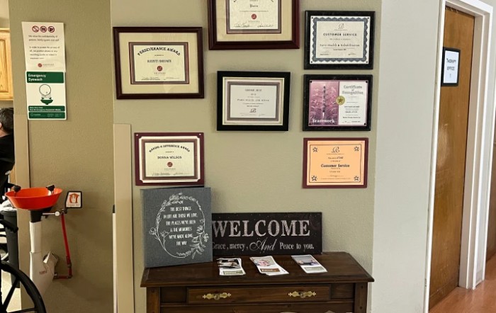A wall featuring multiple framed certificates and diplomas above a table with a welcome sign.
