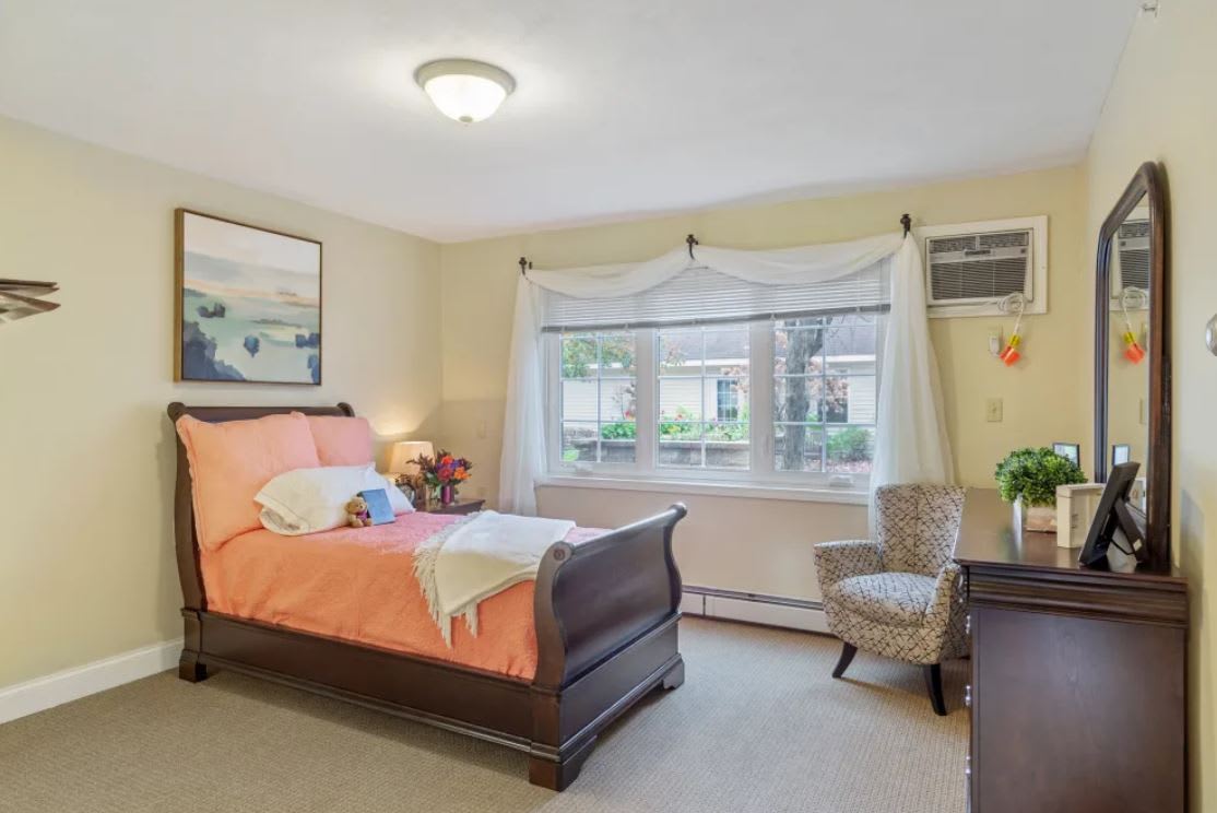 A cozy bedroom with a wooden bed, a chair by the window, and wall decor.