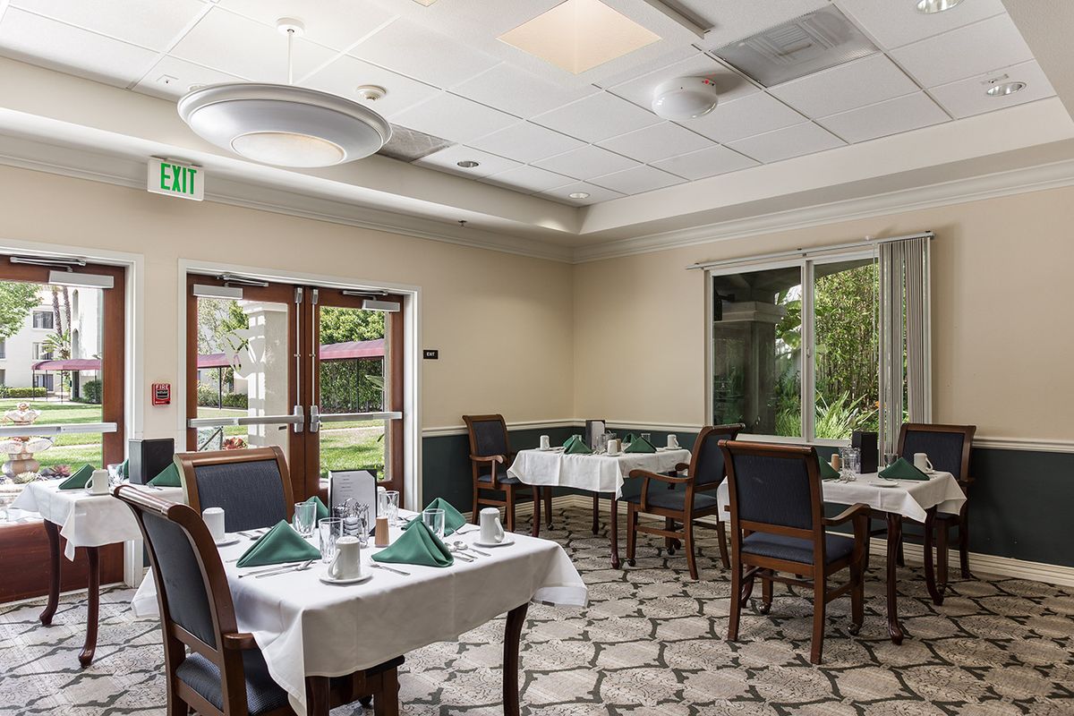 A cozy dining area with neatly set tables and chairs, featuring large windows and elegant decor.