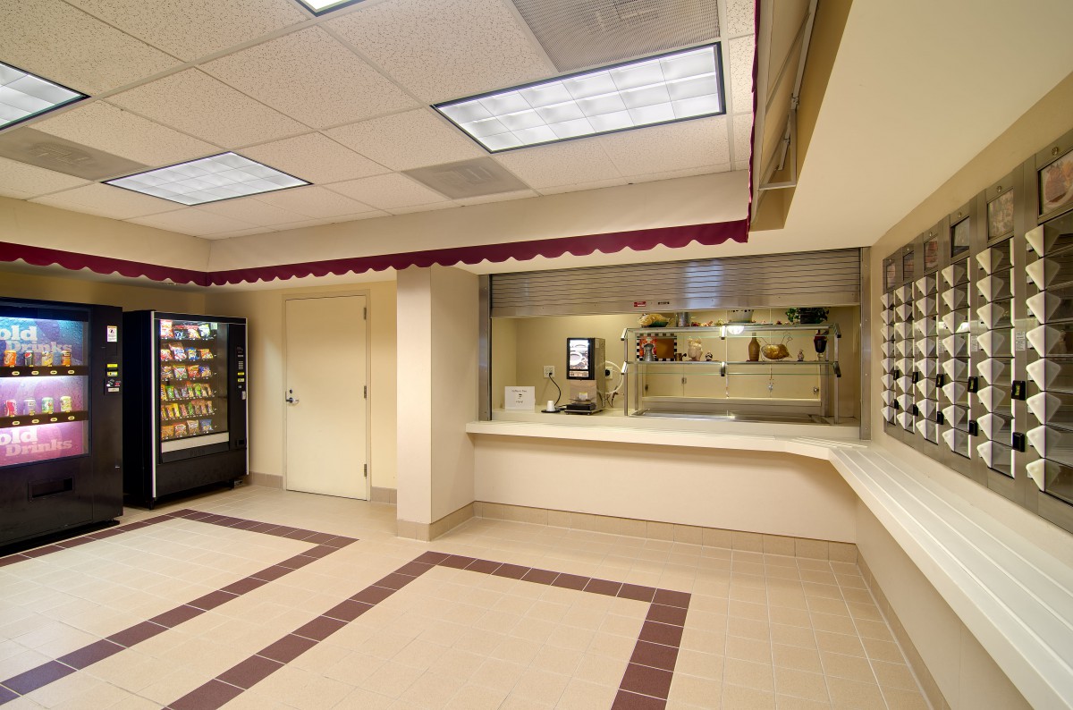 An empty cafeteria with a vending machine and serving counter.