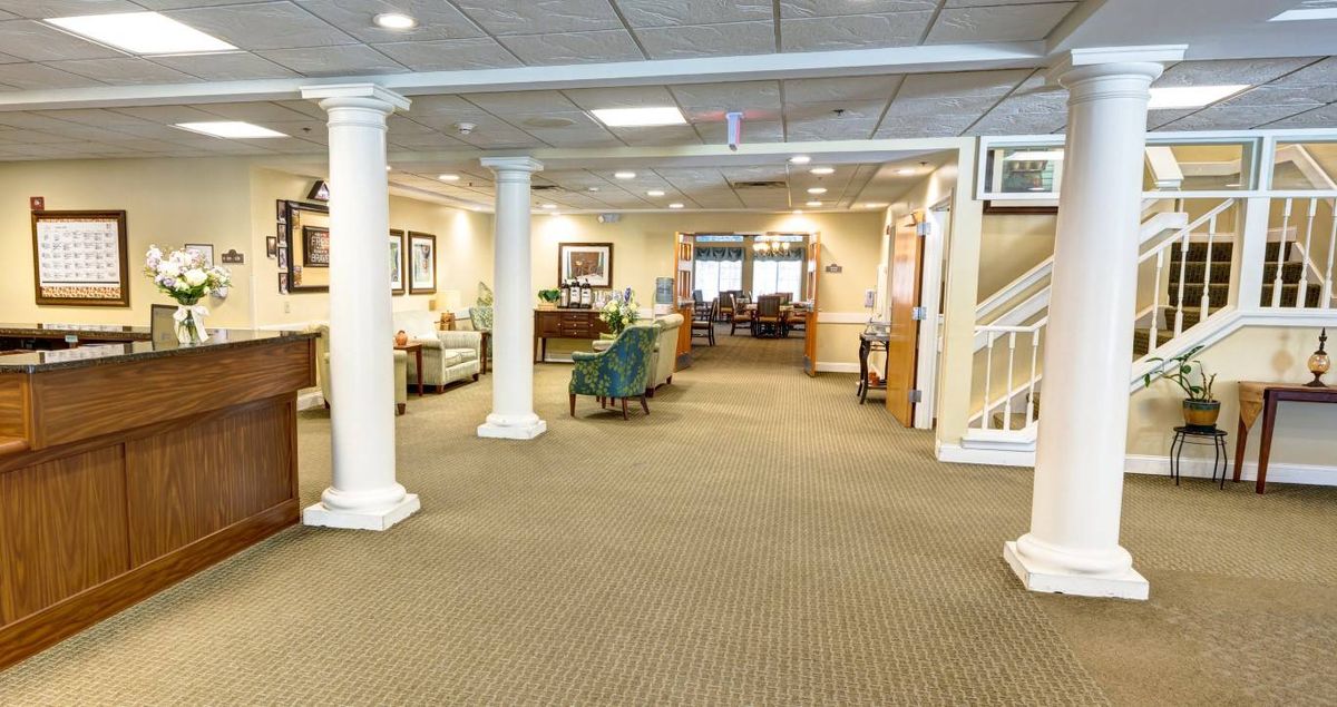 A spacious and well-lit lobby with carpeted flooring, columns, and comfortable furniture.