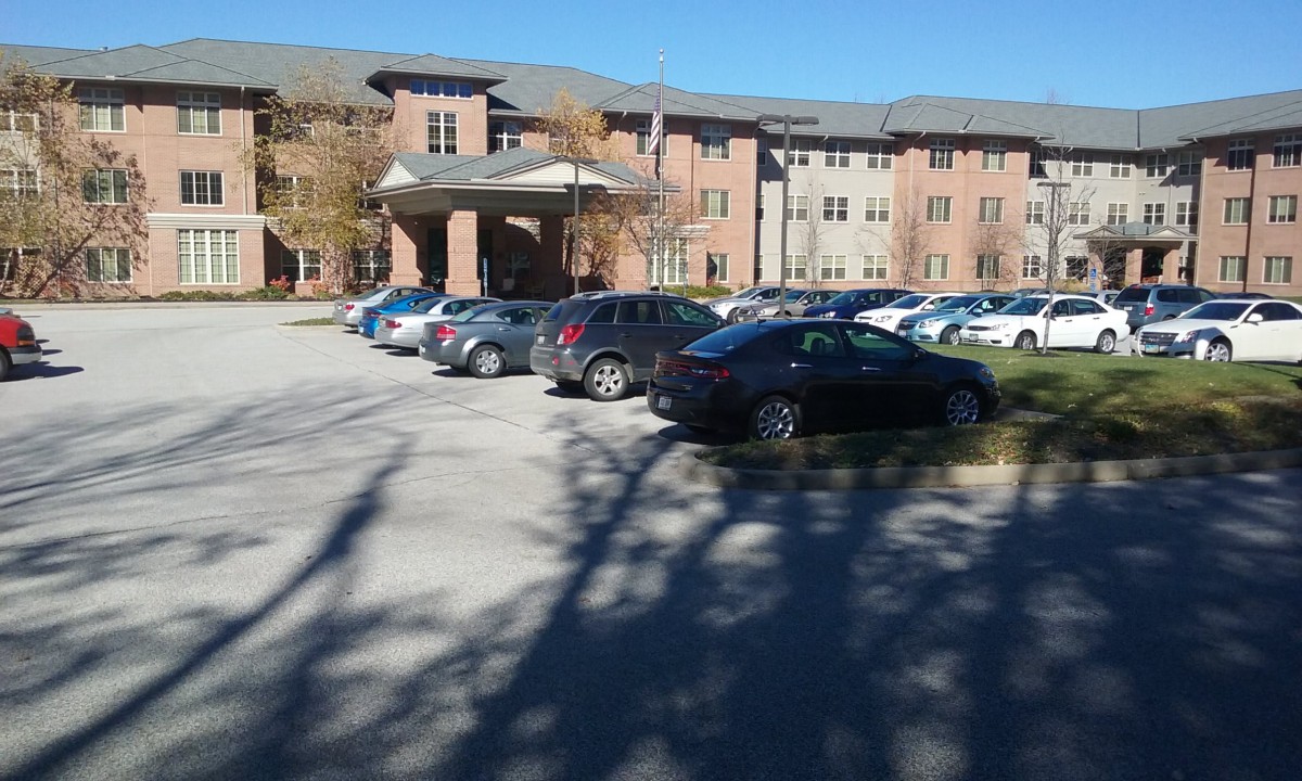 A residential building with a parking lot filled with cars and surrounding trees.