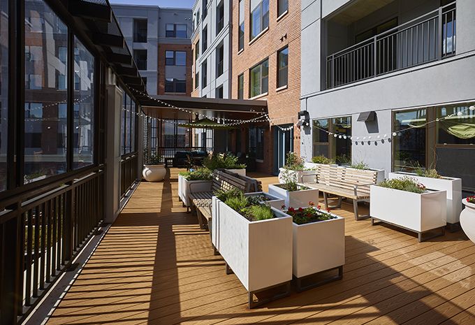 A modern outdoor deck in an apartment complex featuring planters and a seating area.