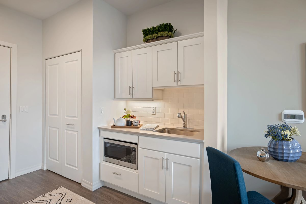 A compact kitchenette with white cabinetry featuring a microwave and sink.
