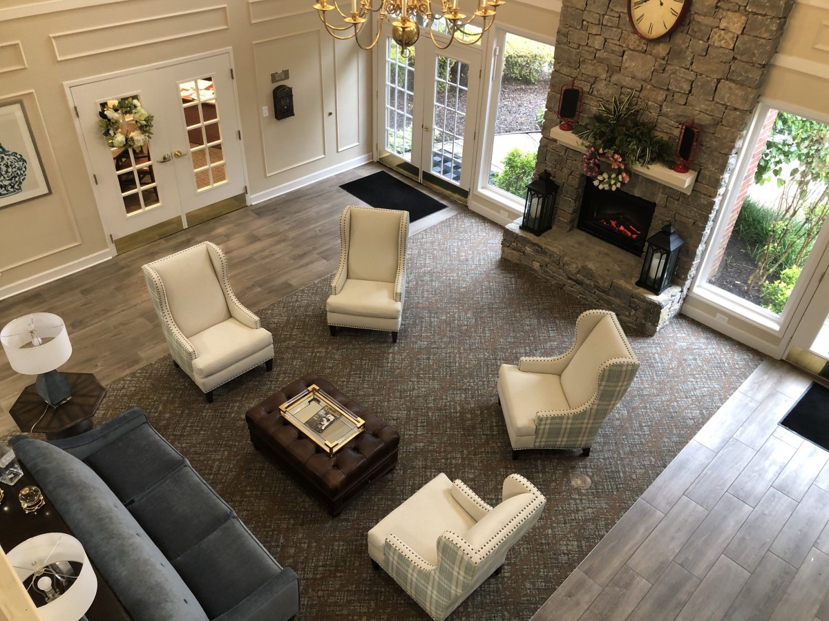An elegant living room featuring a seating arrangement of white chairs and a couch around a central coffee table, with a stone fireplace and large windows providing ample light.