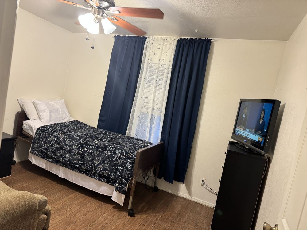 A cozy bedroom featuring a single bed, ceiling fan, and television.