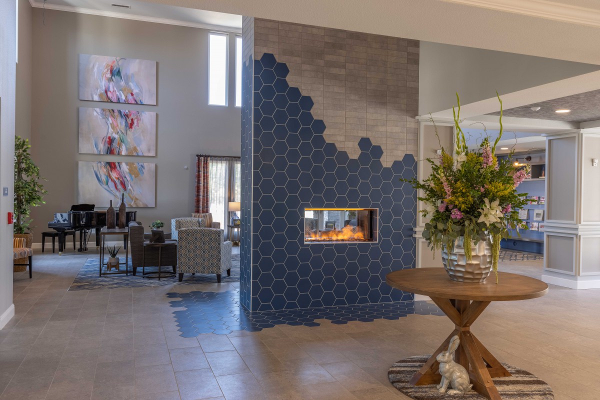A modern living room with a stylish fireplace surrounded by blue tiles and decorated with artwork and a flower arrangement.