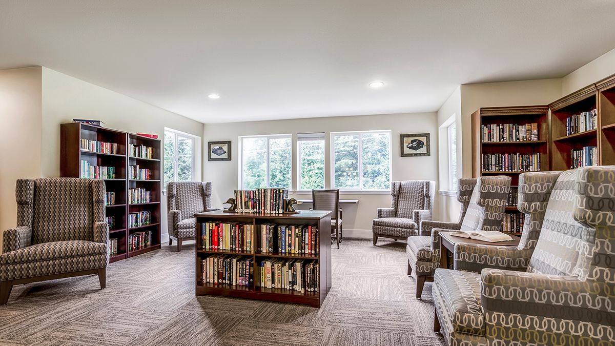 A cozy library reading area with bookshelves, comfortable chairs, and large windows letting in natural light.