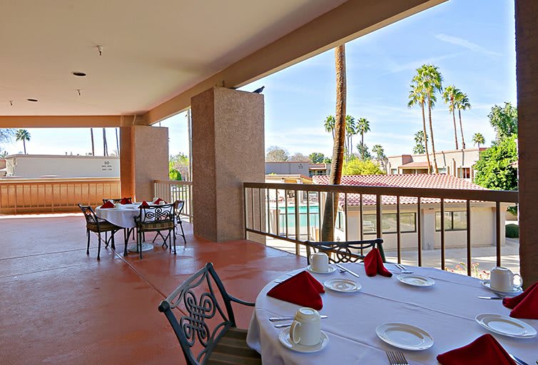 An outdoor dining area with tables set elegantly, overlooking a pool and palm trees.