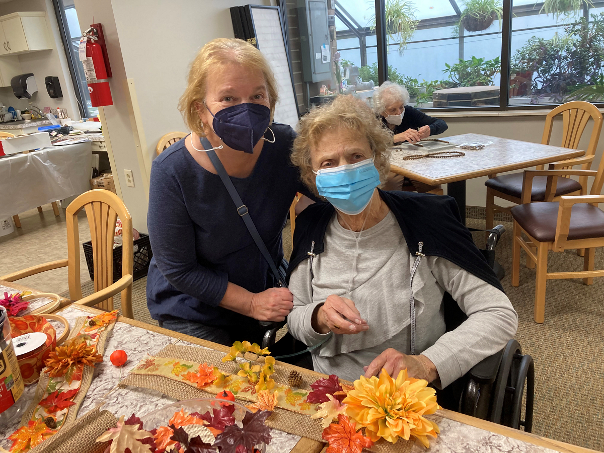 Two people wearing masks work on crafting autumn decorations indoors.