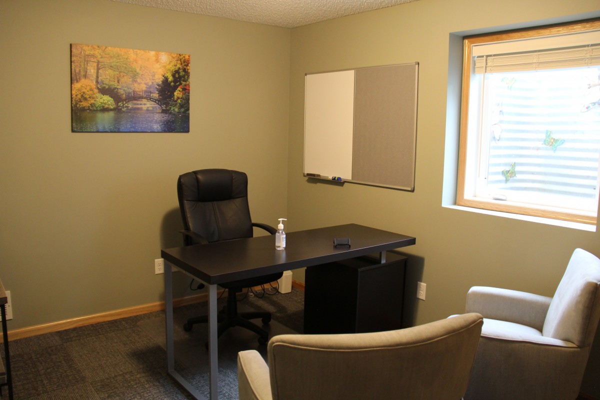 A tidy office with a desk, chairs, and a painting on the wall.