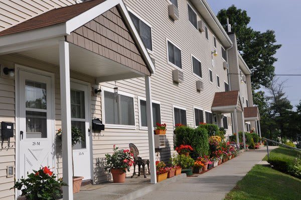 A view of a residential apartment building with well-maintained landscaping and a sidewalk.