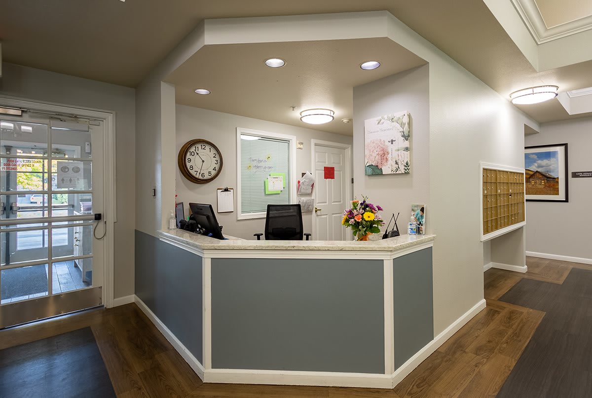 A modern reception area with a desk, flowers, and a clock on the wall.