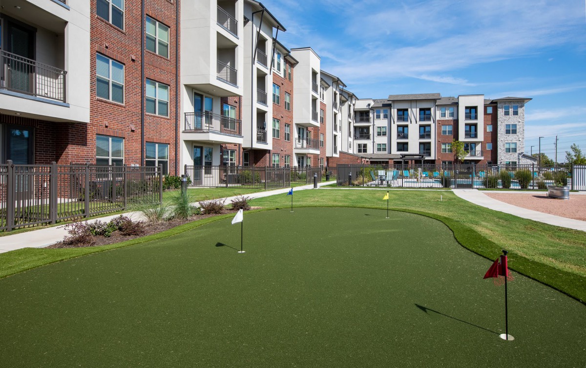 A modern apartment complex featuring a well-maintained putting green for residents.