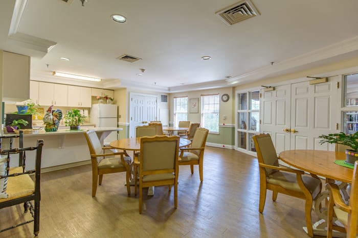 A bright and spacious dining area with multiple tables and chairs, adjacent to a modern kitchen.