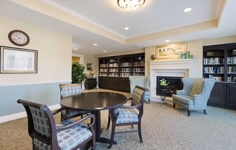 A cozy library with a round table, chairs, and a fireplace surrounded by bookshelves.