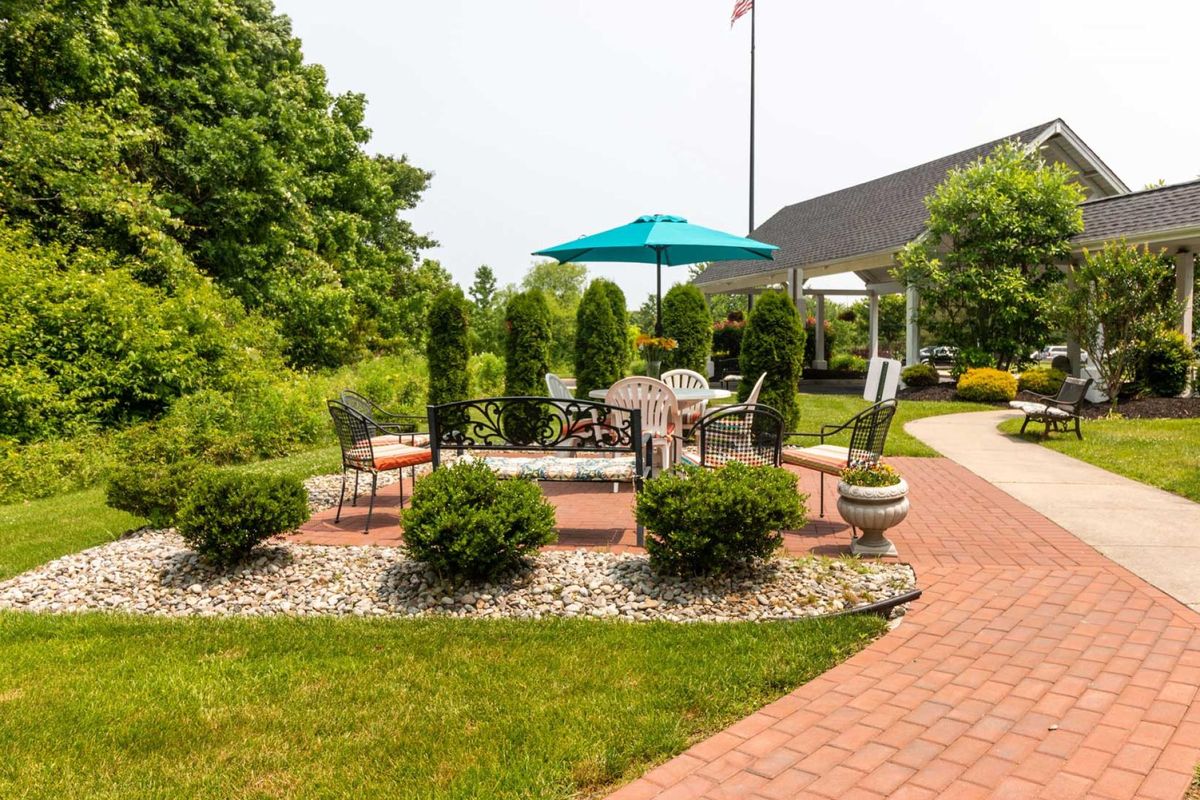 A cozy outdoor patio area surrounded by greenery and featuring a shaded umbrella and seating.