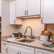 A modern kitchen with white cabinets and a clean countertop featuring a sink and various cooking utensils.