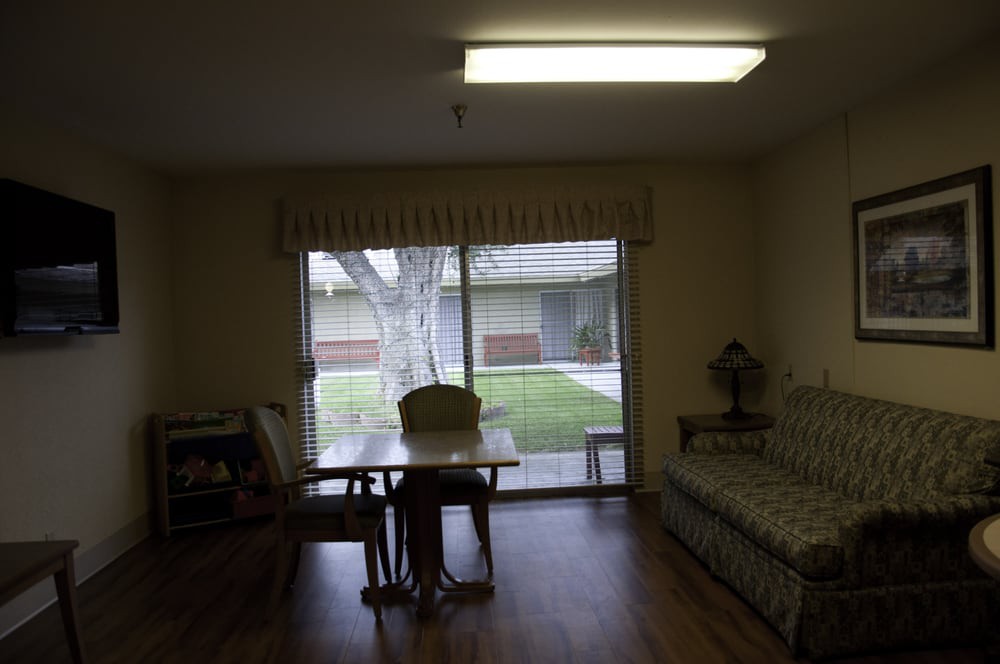 A cozy room interior with a table and chairs next to a large window overlooking a courtyard.