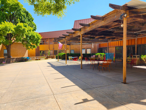 A sunny outdoor courtyard featuring a patio area with seating and surrounding greenery.