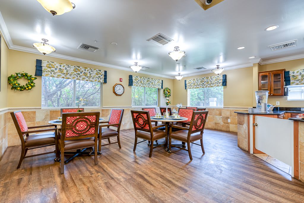 A bright dining area with wooden floors, tables, and chairs, illuminated by ceiling lights.